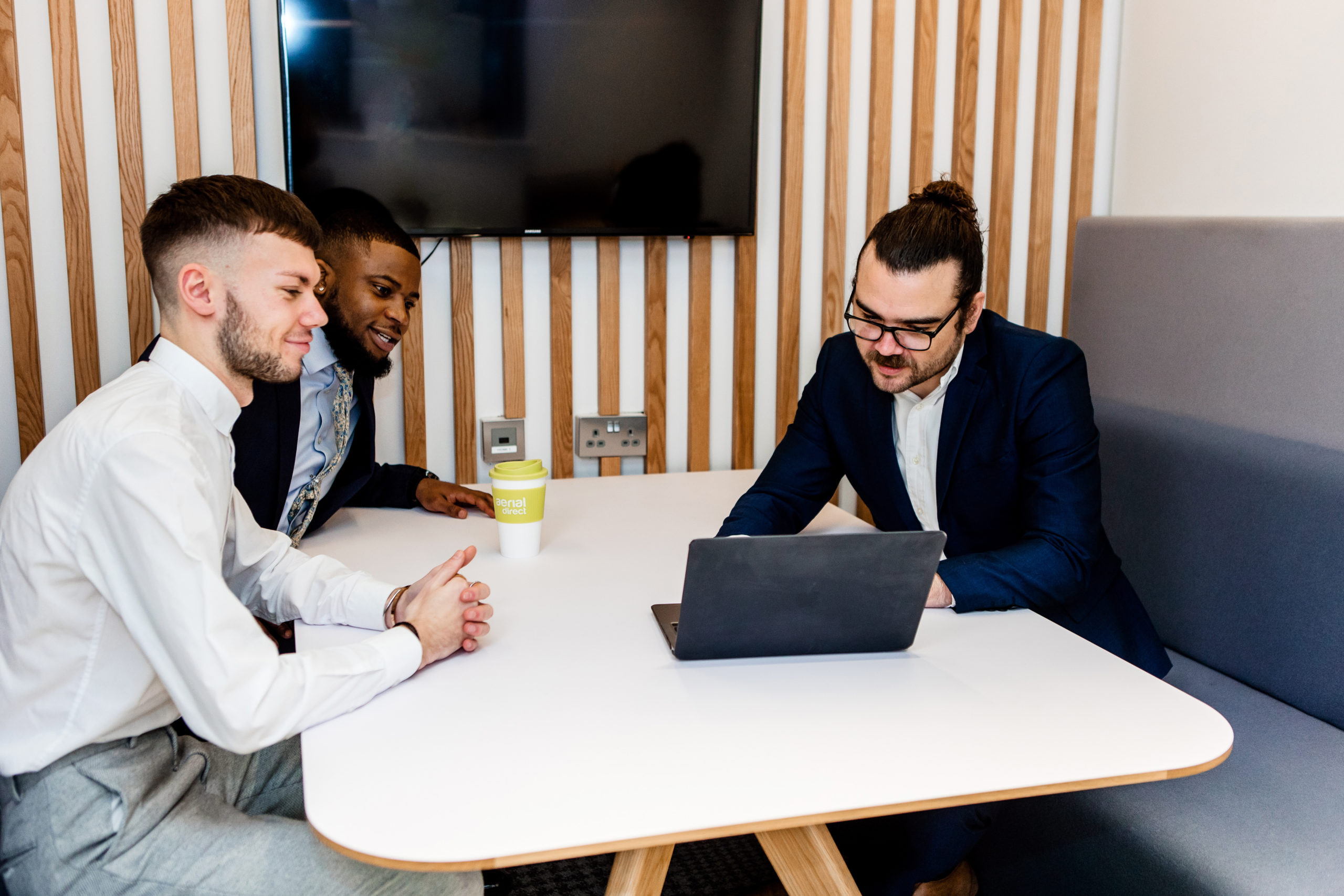 three people talking during a meeting whilst one uses a laptop