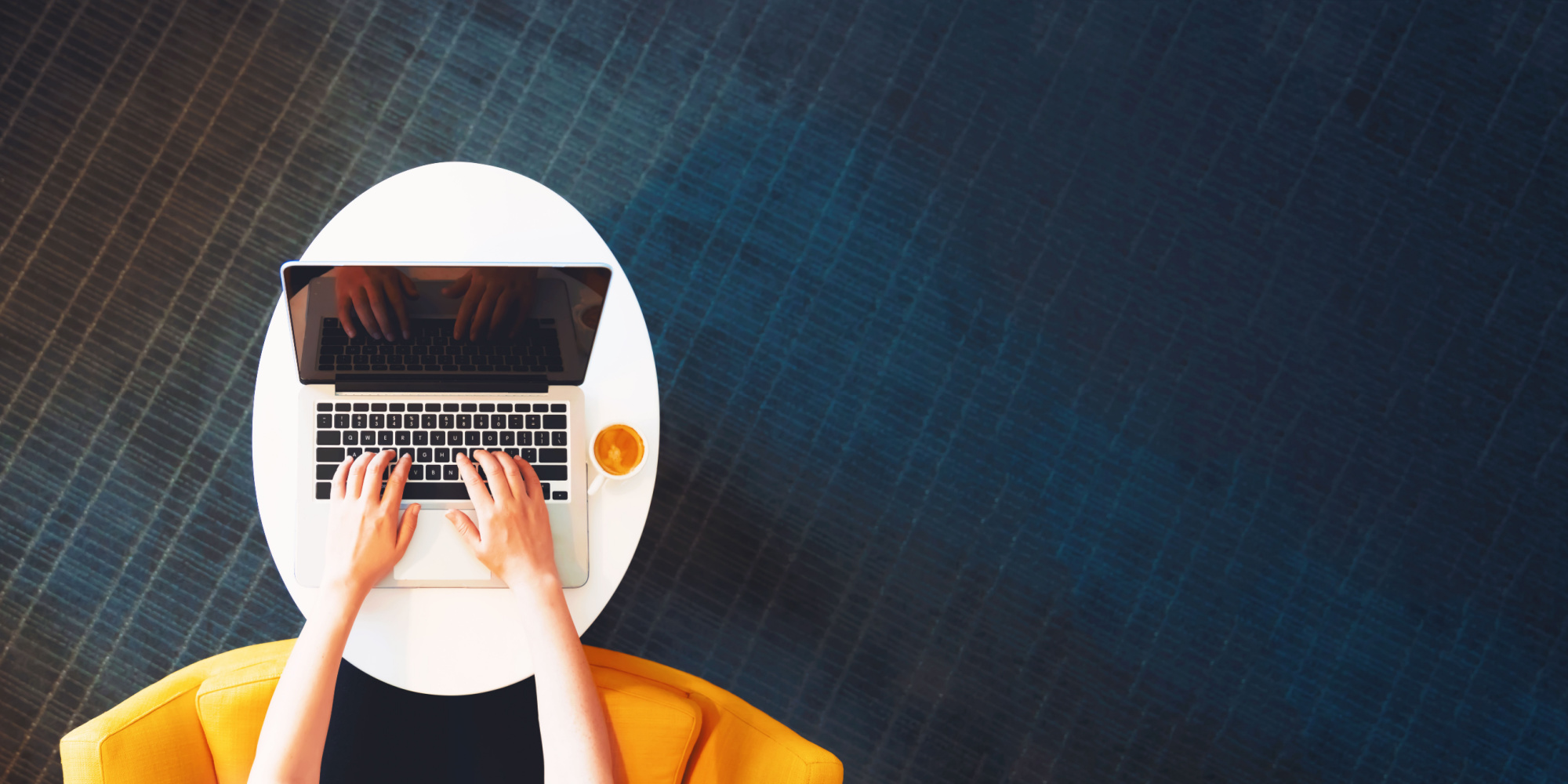 silver laptop resting on a white table with a blue carpet background