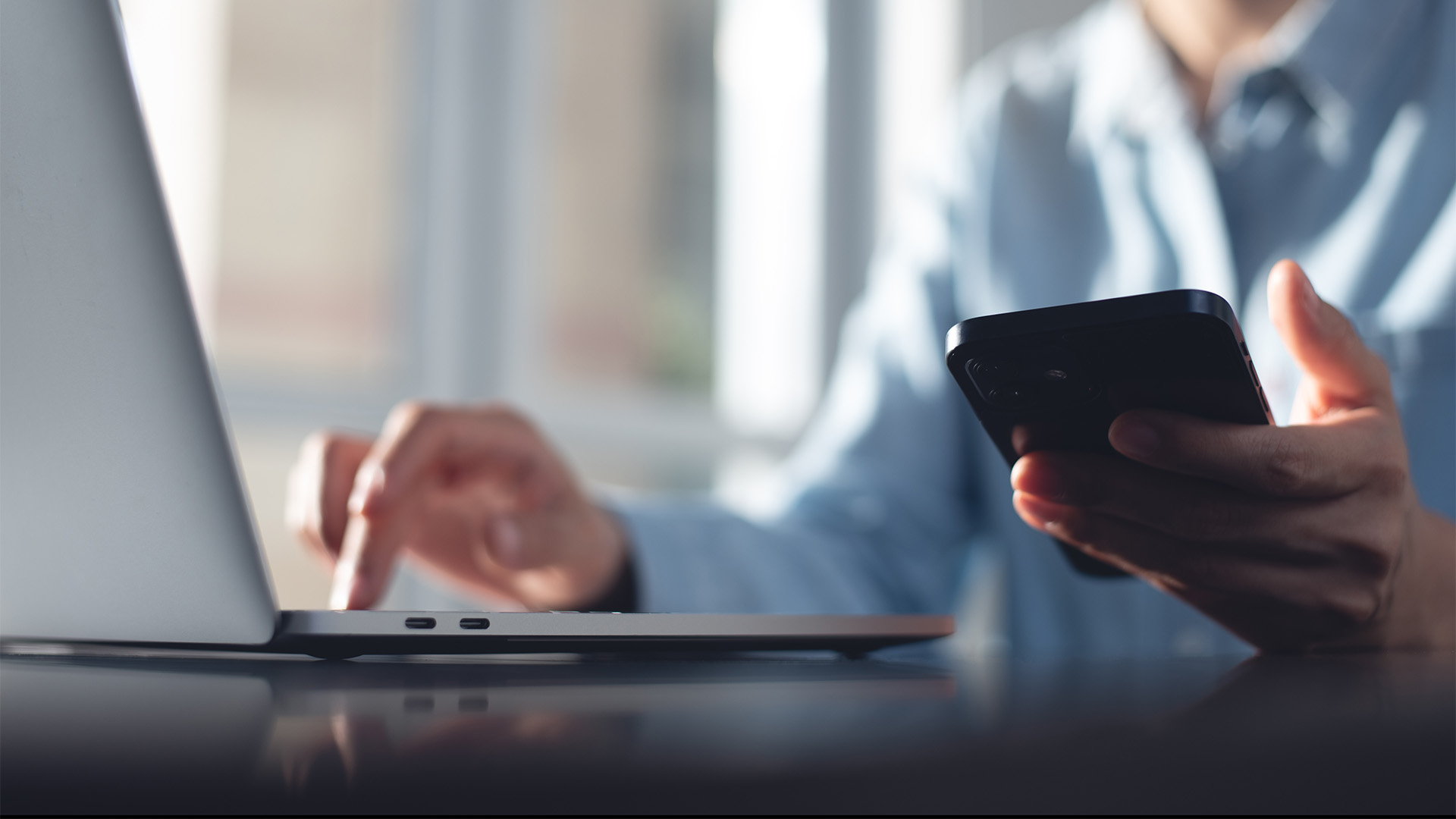 person using a laptop whilst holding a mobile phone