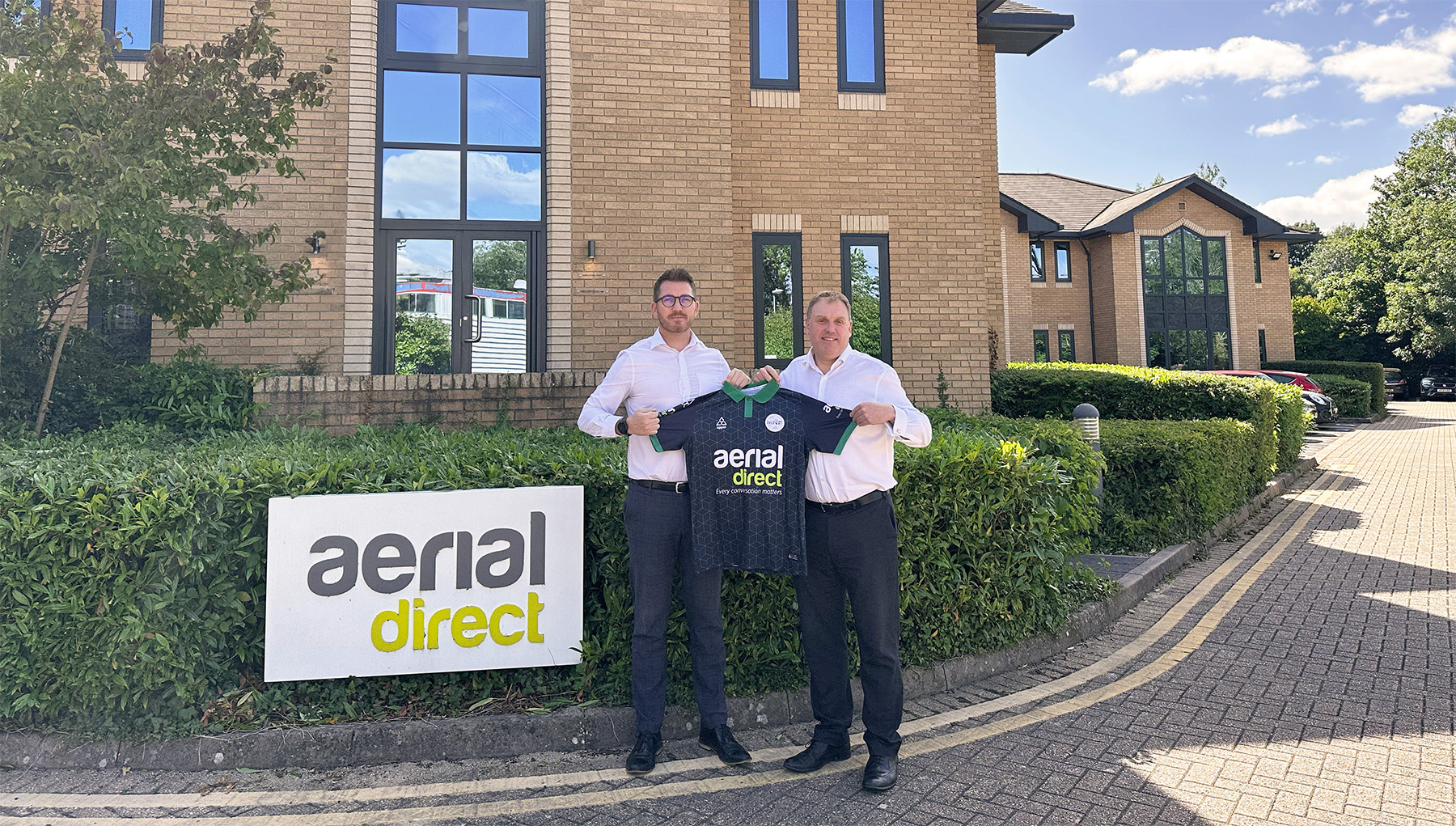 Aerial Direct employees holding a t-shirt with aerial direct logo