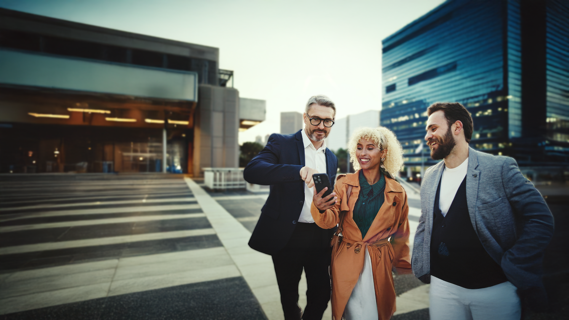three people in a city smiling looking at a mobile phone